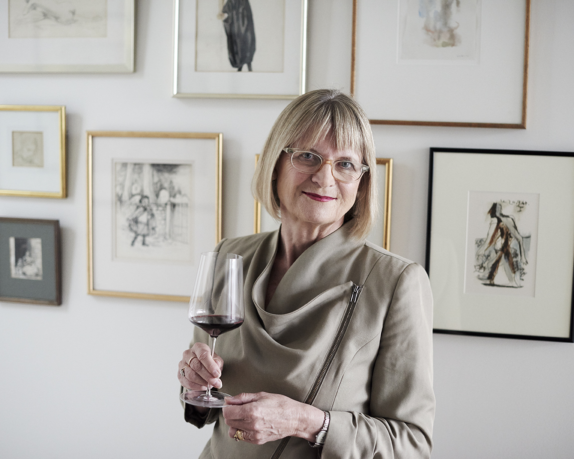 Weinkritikerin Jancis Robinson zuhause im Flur vor Wandbildern mit einem Glas Wein in der rechten Hand