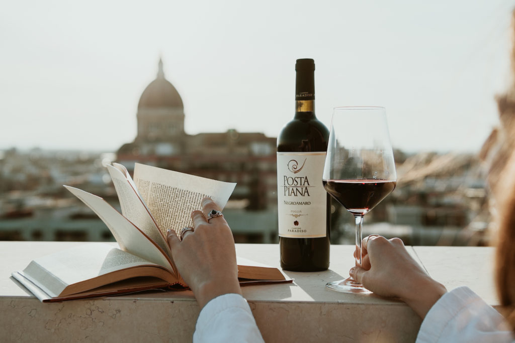 Frau mit Buch und Weinglas und einer Flasche Rotwein an einer Balustrade