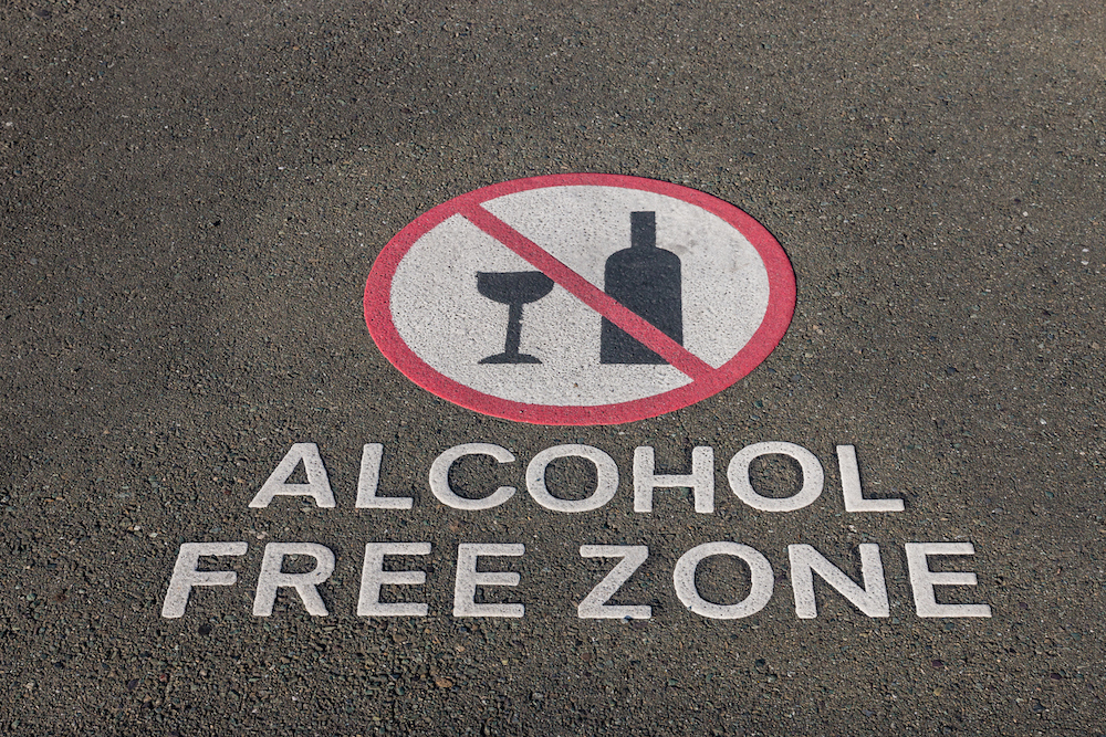 Rundes Verkehrsschild mit einer durchgestrichenen Weinflasche und dem Hinweis Alcohol free zone auf einer Straße
