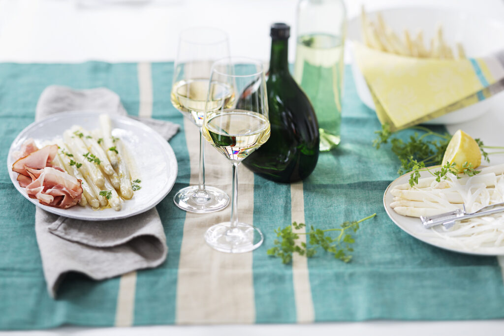 Gedeckter Tisch mit Spargel, Schinken, Weißwein und einem Bocksbeutel