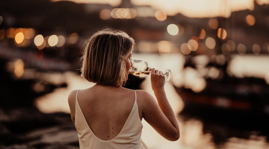 Frau sitzt bei Sonnenuntergang im Sommer an einem Fluss und genießt ein Glas Sommerwein