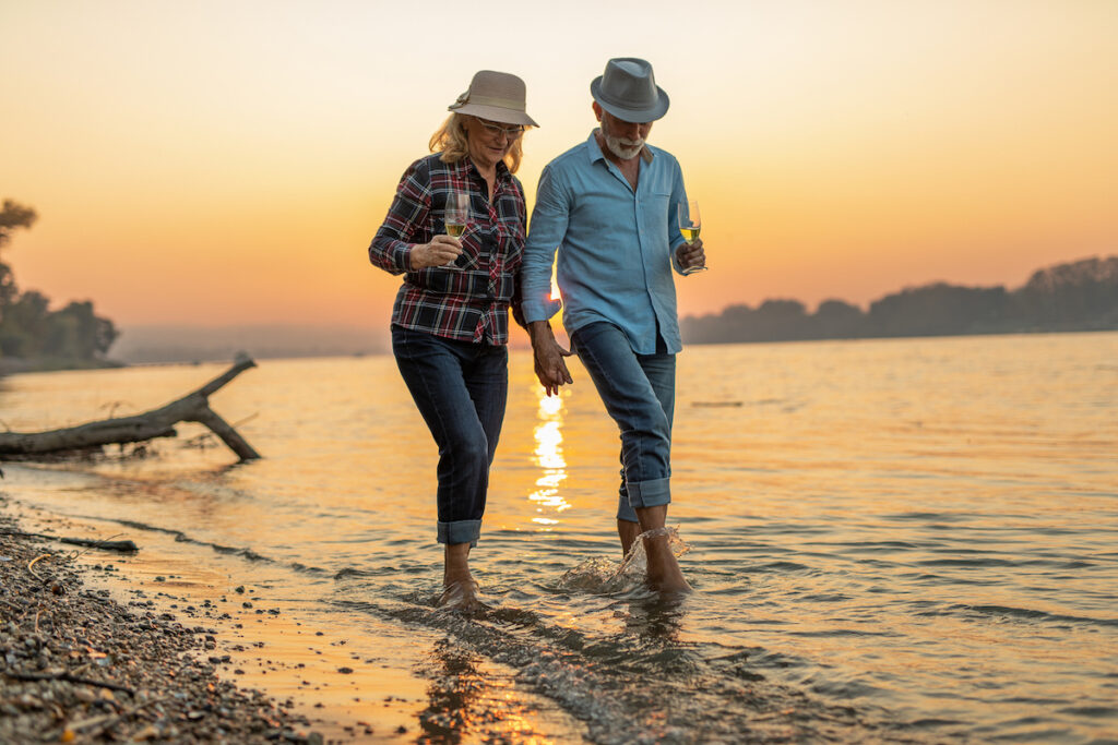 Älteres Paar geht bei Sonnenuntergang im Sommer am Strand spazieren