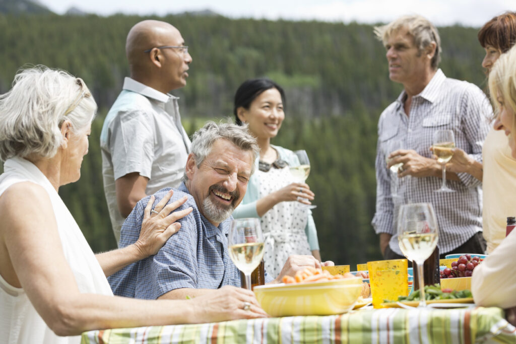 Gruppe von Menschen sitzt draußen an einem Tisch, lacht, isst und genießt Weißwein