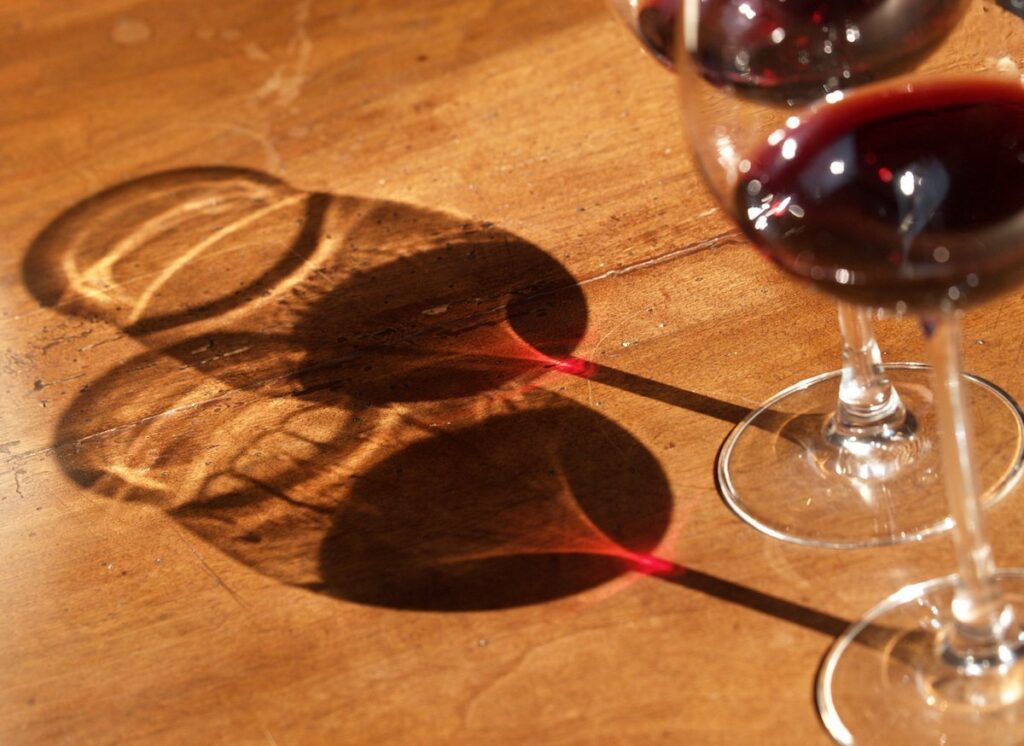 Zwei Rotweingläser auf einem Holztisch, die Schatten werfen
