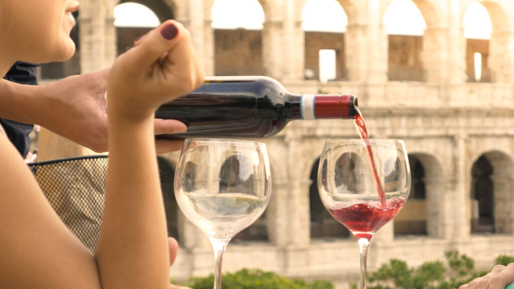 Frau gießt Rotwein mit geschützter Ursprungsbezeichnung mit dem Kolosseum im Hintergrund ein