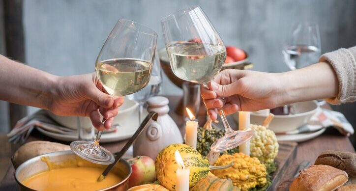 Zwei Menschen stoßen mit Weißwein zu Kürbissuppe an einem herbstlich gedeckten Tisch an