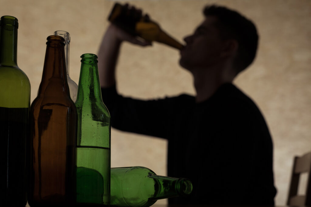 Schatten eines jungen Mannes der Alkohol trinkt, vor ihm stehen und liegen lauter Flaschen