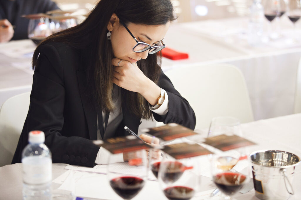Frau verkostet während einer Wein-Fortbildung konzentriert vier Rotweine und macht sich Notizen